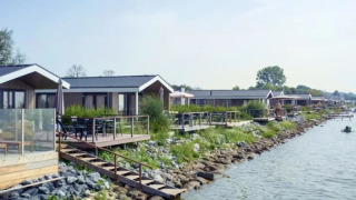 Fila de modernas cabañas junto al lago con terrazas de madera y vegetación junto al agua tranquila.