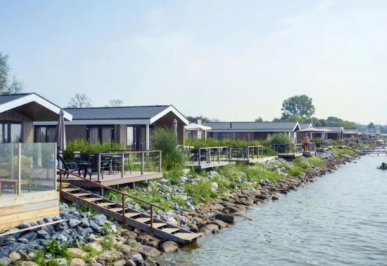 Fila de modernas cabañas junto al lago con terrazas de madera y vegetación junto al agua tranquila.