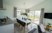 Modern lodge dining area with six chairs, large windows, gray curtains, and a view to a garden patio.