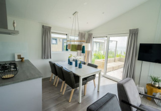 Modern lodge dining area with six chairs, large windows, gray curtains, and a view to a garden patio.