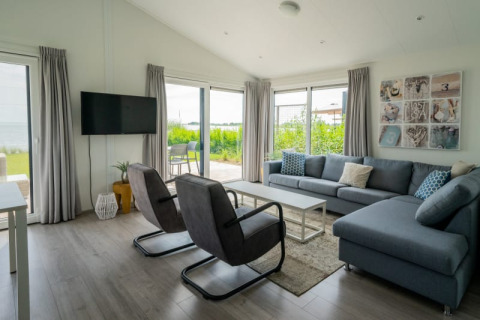 Sala moderna de lodge con grandes ventanales, sofá gris, sillones y vistas al jardín exterior.