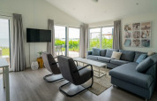 Modern lodge living room with large windows, gray sofa, armchairs, flat TV, and garden view outside.