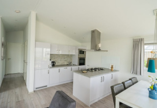 Moderne keuken en eetruimte in een lodge met witte kasten, eettafel en groot raam met gordijnen.