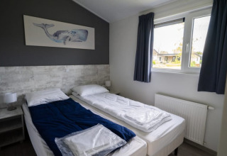 Modern lodge bedroom with two single beds, blue blanket, whale painting on the wall, and large window.
