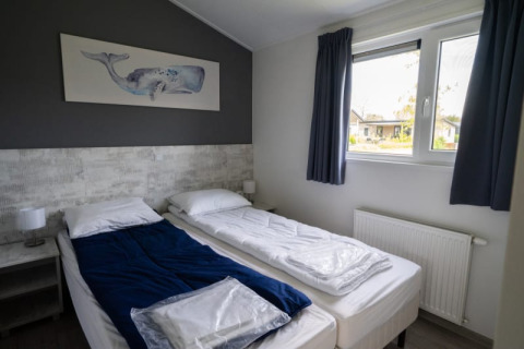 Chambre de lodge moderne avec deux lits simples, couverture bleue, tableau de baleine et grande fenêtre.