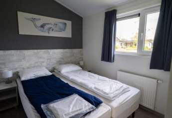 Habitación de lodge moderna con dos camas individuales, manta azul, cuadro de ballena y gran ventana.