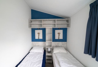 Dos camas individuales en una habitación minimalista de lodge con pared azul y estantería superior.