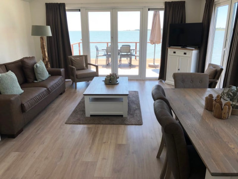 Sala de estar luminosa en una cabaña con muebles modernos, ventanas grandes y vistas al lago y terraza.