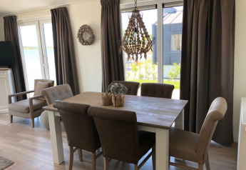 Licht eetgedeelte in een lodge met bruine gordijnen, houten tafel, zachte stoelen en zicht op de tuin.