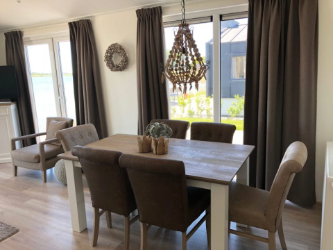 Comedor luminoso en una cabaña con cortinas marrones, mesa de madera, sillas acolchadas y vista al jardín.
