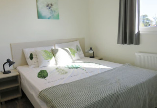 Dormitorio luminoso de una cabaña, cama doble con ropa de cama natural, mesas de noche y ventana.