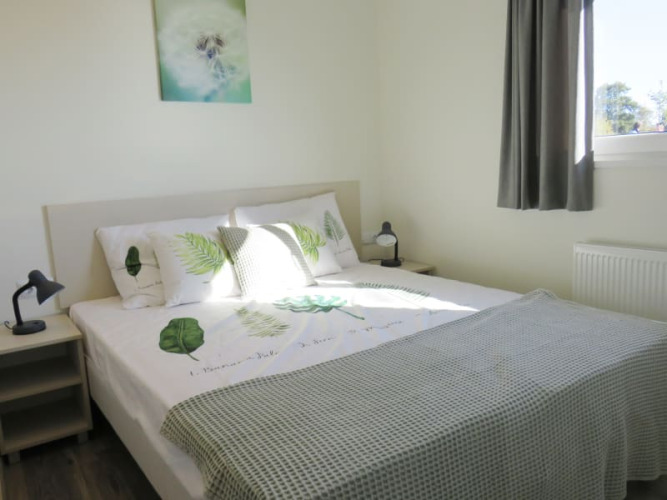 Helles Schlafzimmer in einer Lodge mit Doppelbett, naturgemusteter Bettwäsche, Nachttischen und Fenster.