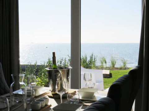View from a lodge of a set table with wine, glasses, and ocean scenery visible through large windows.