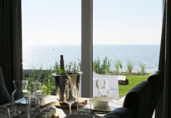 Zicht vanuit een lodge op een gedekte tafel met wijn, glazen en zeezicht door hoge ramen.