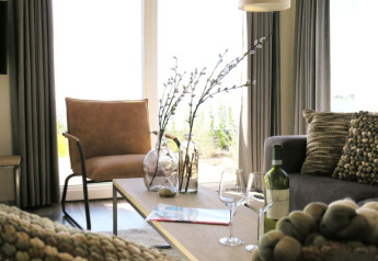 Soggiorno moderno in una lodge con grandi finestre, poltrona marrone, cuscini, vino e due calici.