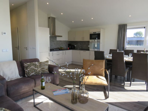 Modern lodge living space with open kitchen, dining table, cozy seating, and sunlight through window.