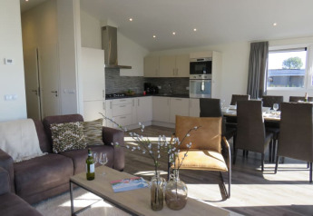 Moderne lodge-stue med åbent køkken, spisebord, komfortable møbler og sollys gennem vinduet.