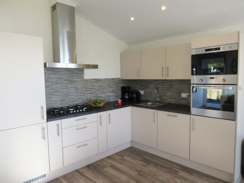 Modern lodge kitchen with light cabinets, grey tiled backsplash, gas hob, built-in ovens, and appliances.
