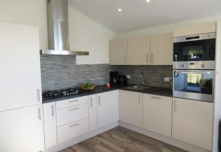 Moderne lodgekeuken met lichte kasten, een grijze tegelwand, gaskookplaat en ingebouwde ovens.