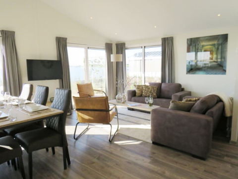 Lichte, gezellige woonkamer in een lodge met moderne eettafel, comfortabele zetels en grote ramen.