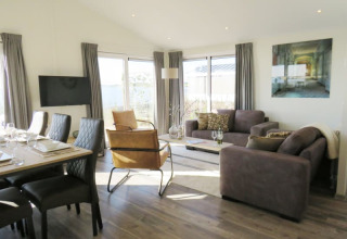 Lichte, gezellige woonkamer in een lodge met moderne eettafel, comfortabele zetels en grote ramen.