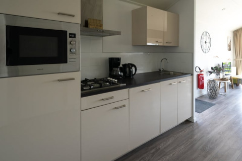 Modern lodge kitchen featuring a stove, microwave, coffeemaker, sink, and a bright living area beyond.