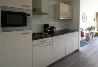 Cuisine moderne dans un lodge avec cuisinière, micro-ondes, cafetière et salon lumineux visible.