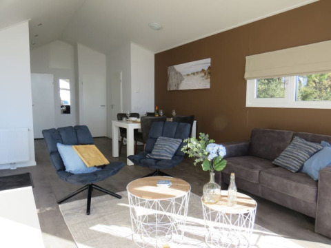 Lodge woonkamer met moderne blauwe stoelen, grijze bank, witte tafels en veel daglicht door ramen.