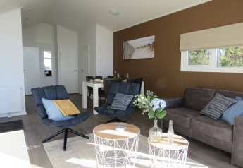 Gemütliches Wohnzimmer einer Lodge mit modernen Sesseln, Sofa, Esstisch und großem Fensterblick.