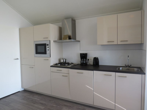 Cocina moderna en una cabaña con gabinetes blancos, microondas, cafetera y fregadero de acero inoxidable.