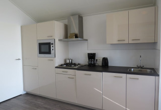 Cocina moderna en una cabaña con gabinetes blancos, microondas, cafetera y fregadero de acero inoxidable.