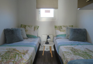 Acogedora habitación de lodge con dos camas individuales, cojines mullidos y una mesa redonda pequeña con lámpara.