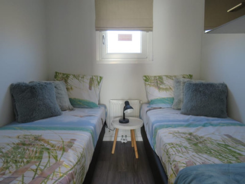 Sfeervolle lodgekamer met twee eenpersoonsbedden, sierkussens en een klein rond tafeltje met lampje.