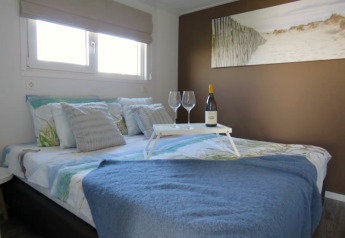 Gezellige lodge slaapkamer met wijn, glazen op een dienblad, blauw deken en strandfoto boven het bed.
