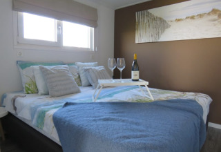 Camera accogliente in un lodge con vino e calici sul vassoio, coperta blu e quadro della spiaggia.