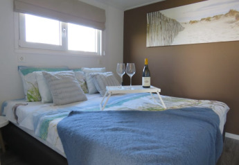 Cozy lodge bedroom with wine and glasses on a tray, blue blanket, and beach artwork above the bed.