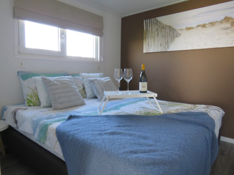 Cozy lodge bedroom with wine and glasses on a tray, blue blanket, and beach artwork above the bed.