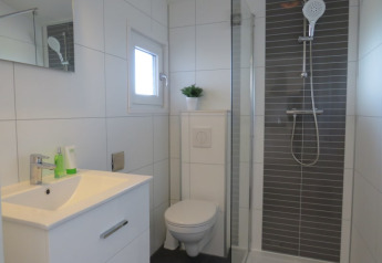 Baño moderno en una cabaña con ducha, inodoro, lavabo, espejo, ventana pequeña y planta decorativa.