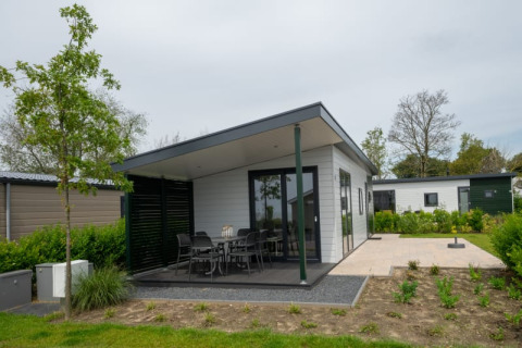 Moderne lodge met overdekt terras, buiteneethoek en tuin, omringd door groen en bomen.