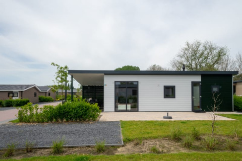 Moderne lodge met plat dak en grote ramen, omgeven door groen en soortgelijke huisjes in de buurt.