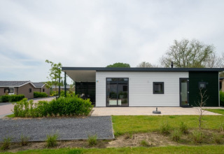 Moderne lodge met plat dak en grote ramen, omgeven door groen en soortgelijke huisjes in de buurt.