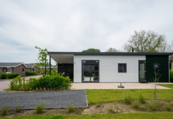 Modern lodge with a flat roof and large windows, surrounded by greenery and with similar houses nearby.