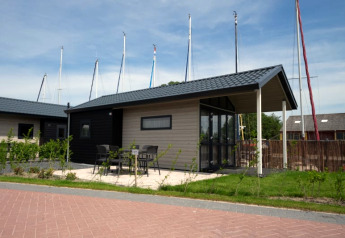 Lodge moderne avec terrasse, table et chaises, situé près de yachts avec mâts visibles en arrière-plan.