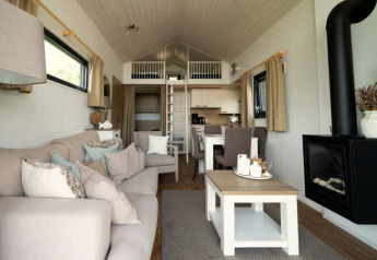 Intérieur de lodge moderne avec canapé, cheminée, salle à manger, cuisine ouverte et mezzanine accessible.