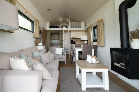 Moderne lodge med hyggelig stue, sofa, ildsted, spisebord, åbent køkken og hems med stige.