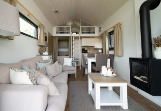 Intérieur de lodge moderne avec canapé, cheminée, salle à manger, cuisine ouverte et mezzanine accessible.