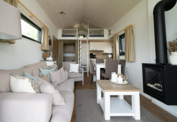 Moderne lodge med hyggelig stue, sofa, ildsted, spisebord, åbent køkken og hems med stige.