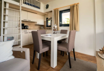 Intérieur de lodge moderne avec table à manger, quatre chaises, kitchenette, mezzanine et fenêtre.