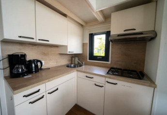 Petite cuisine de lodge moderne avec armoires blanches, cuisinière à gaz, cafetière et fenêtre éclairée.