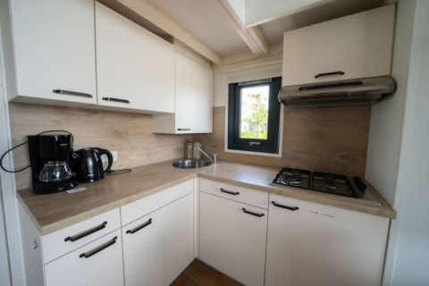 Moderne lodgekeuken met witte kasten, gaskookplaat, koffiemachine en een klein raam met uitzicht.